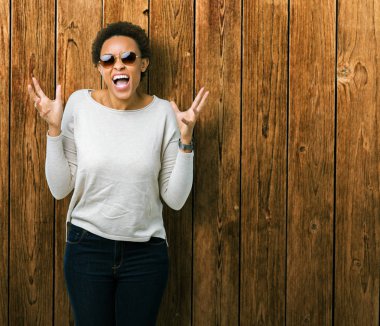 Güzel genç Afro-Amerikan kadın üzerinde güneş gözlüğü takıyor arka plan deli izole ve deli bağırarak ve agresif ifade ve silah kaldırdı bağırıyor. Hayal kırıklığı kavramı.