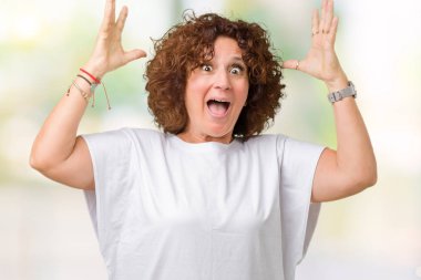 Üzerinde beyaz t-shirt giyen güzel orta ager üst düzey kadın deli kutluyor arka plan izole ve başarı için kaldırdı kollarını açarak hayrete ve heyecanlı çığlık gözleri açık. Kazanan kavramı