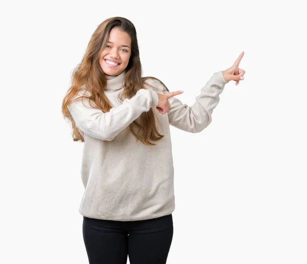 笑顔で側に つの手と指で指しているカメラを見て孤立の背景にタートルネックのセーターを着ている若い美しいブルネットの女性 — ストック写真