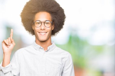 Afro saçlı gösterilen ve kendinden emin ve mutlu gülümseyen bir parmak ile işaret eden oktan yukarı gözlüklü genç Afro-Amerikan adam.