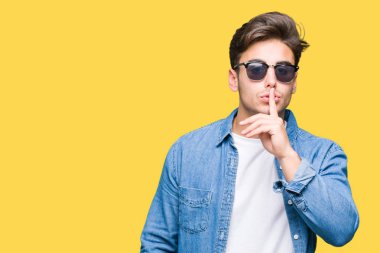 Genç yakışıklı adam dudaklarında parmak ile sessiz olmanı izole arka plan üzerinde güneş gözlüğü takıyor. Sessizlik ve gizli kavramı.