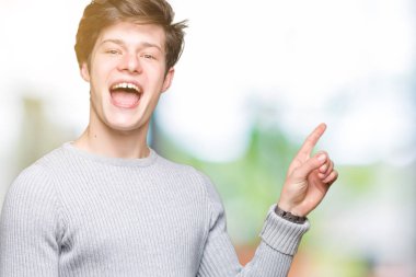 Kameraya bakarak yan el ve parmak ile işaret yüzünde kocaman bir gülümseme ile izole arka plan üzerinde kış kazak giyen genç yakışıklı adam.