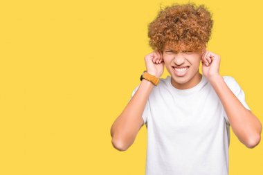 Casual beyaz t-shirt kapsayan kulakları parmakları ile yüksek sesle müzik gürültü rahatsız ifade ile giyen afro saçlı Genç yakışıklı adam. Sağır kavramı.