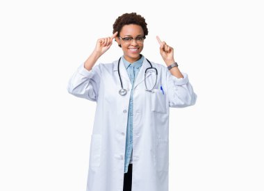 Genç Afrikalı Amerikan doktor kadın izole arka plan üzerinde tıbbi ceket giyen her iki el parmak, büyük bir fikir veya düşünce, iyi bellek ile kafa işaret gülümseyen