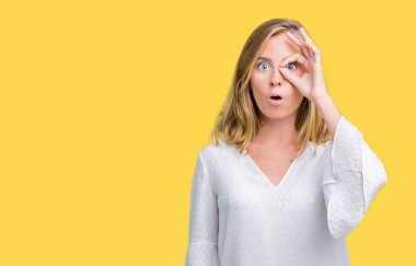 Beautiful young elegant woman over isolated background doing ok gesture shocked with surprised face, eye looking through fingers. Unbelieving expression.