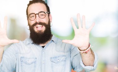 Uzun saç ve sakal gösterilen ve parmakları ile işaret gözlüklü genç hipster adamla kendinden emin ve mutlu gülümseyerek süre on numara.