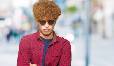 Yakışıklı genç afro saçlı güneş gözlüğü şüpheci ve sinir, onaylamayan ifade yüz çapraz kollu giyiyor. Negatif kişi.