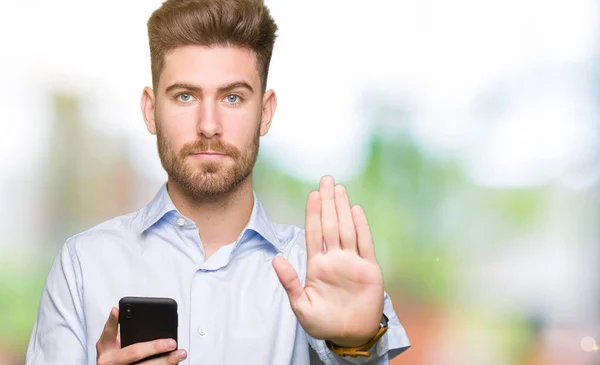 年轻英俊的男人业务使用智能手机与开放的手做停止标志与严肃和自信的表情 防御手势 — 图库照片