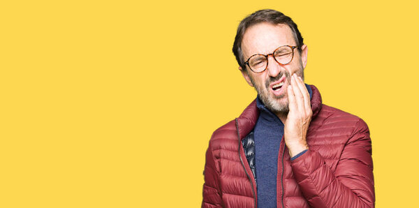 Middle age handsome man wearing glasses and winter coat touching mouth with hand with painful expression because of toothache or dental illness on teeth. Dentist concept.
