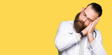 Uyku yorgun hayal ve ile gülümseyen gözleri kapalı iken ellerle birlikte poz tıbbi bir palto giyiyor sakallı genç sarışın doktor adam.