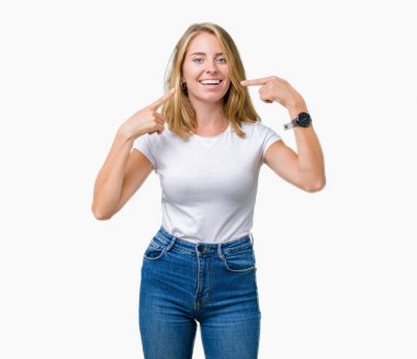Kendinden emin gösterilen ve işaret parmakları diş ve ağız ile gülümseyen izole arka plan üzerinde rahat beyaz t-shirt giyen güzel ve genç birbayan. Sağlık kavramı.