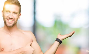 Çıplak göğüs gösteren yakışıklı gömleksiz adam palmiye el gösteren ve başparmak ile ok jest yapıyor, mutlu ve neşeli gülümseyen