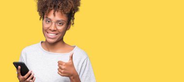 Ok işareti, başparmak ile parmak, mükemmel işareti yapıyor kocaman bir gülümseme ile izole arka plan üzerinde mutlu Smartphone kullanan genç Afro-Amerikan kadın