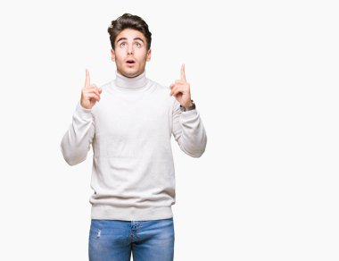 Yakışıklı delikanlı izole arka plan üzerinde boğazlı kazak giyen hayrete ve yukarıya bakıyor ve parmakları ile işaret ve silah kaldırdı şaşırttı.