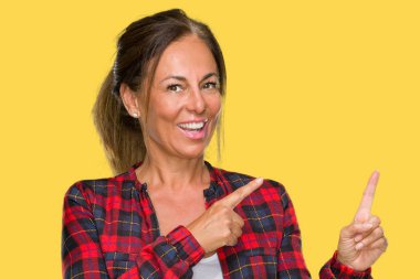 Orta yaş yetişkin kadın gülümseyerek ve iki elleri ve parmakları ile tarafına işaret kamera bakarak izole arka plan üzerinde rahat ceket.