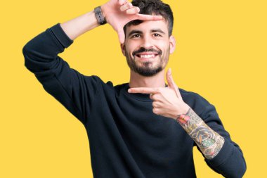 Yakışıklı delikanlı elle yapma çerçeve ve parmakları ile mutlu yüz gülümseyen izole arka plan üzerinde. Yaratıcılık ve Fotoğrafçılık kavramı.