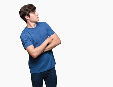 Genç yakışıklı adam üzerinde mavi t-shirt giyen izole arka plan ile yan bakarak gülümseyen ikna ve emin geçti