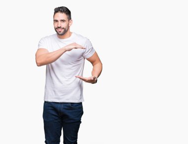 Genç adam, büyük ve büyük boyutlu işareti gösteren eller ile izole arka planda işaret üzerinde rahat beyaz t-shirt giyiyor, ölçmek sembolü. Kameraya bakarak gülümsüyor. Ölçme konsepti.