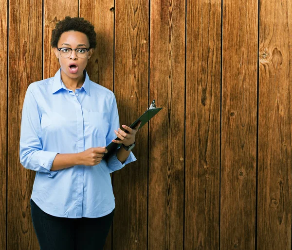 Young african american businesss woman holding clipboard over isolated background scared in shock with a surprise face, afraid and excited with fear expression