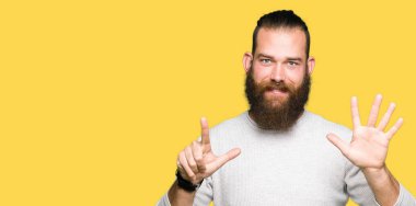 Genç sarışın adam rahat kazak gösteren ve parmak sayısı yedi ile işaret giymiş iken emin ve mutlu gülümseyen.