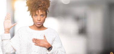 Üzerinde kış kazak giyen güzel genç Afro-Amerikan kadın izole arka plan göğüs ve bir sadakat sözü yemin yapma avuç, el ile küfür