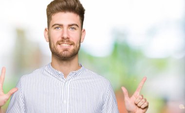 Genç ve yakışıklı bir adam kendini beğenmiş ve mutlu bir şekilde gülümserken yedi numaralı parmaklarıyla onu işaret ediyor..