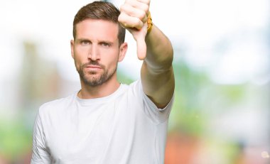 Yakışıklı adam rahat beyaz t-shirt mutsuz ve öfkeli gösteren reddetme ve başparmak aşağı jest ile negatif görünümlü giyiyor. Kötü ifade.