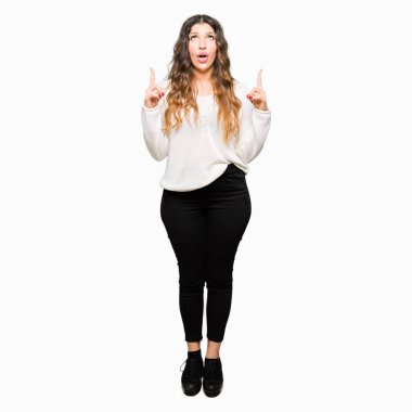 Beyaz kazak giyen genç güzel kadın şaşırttı ve yukarı bakarak ve parmakları ile işaret ve kollarını kaldırdı şaşırttı.