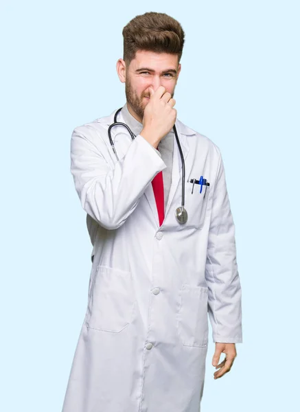 Young Handsome Doctor Man Wearing Medical Coat Smelling Something Stinky — Stock Photo, Image