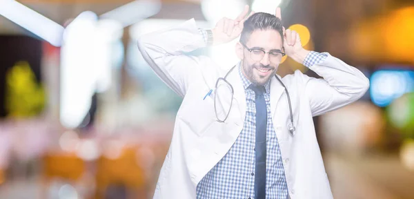 Handsome young doctor man over isolated background Posing funny and crazy with fingers on head as bunny ears, smiling cheerful