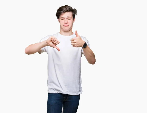 年轻英俊的男人穿着休闲白色 T恤在孤立的背景做大拇指向上和向下 分歧和同意表达 疯狂的冲突 — 图库照片
