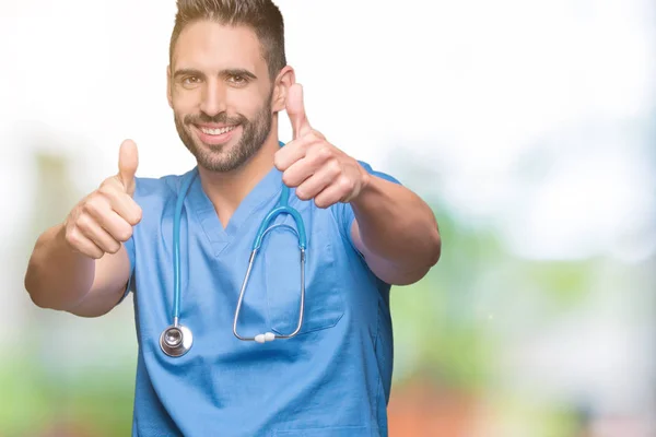 ハンサムな若い医者の外科医男の手で肯定的なジェスチャーをして承認する分離の背景の上の親指を笑顔と幸せな成功のため カメラ 勝者のジェスチャーを見てください — ストック写真