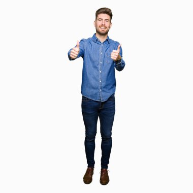 Genç yakışıklı sarışın adam el ile olumlu jest yapıyor onaylayan rahat kot gömlek giyen, gülümseyerek kadar başparmak ve başarı için mutlu. Kameraya bakmak, kazanan jest.