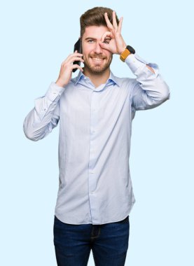 Genç yakışıklı adam iş Smartphone mutlu yüz el parmaklarının arasından seyir göz üzerinde ok işaretiyle yapıyor gülümseyerek konuşuyor