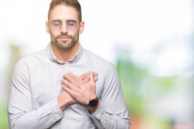 Yakışıklı delikanlı ile gülümseyen izole arka plan üzerinde güneş gözlüğü takıyor kapalı gözler ve yüzünde minnettar jest ile göğüs üzerinde eller. Sağlık kavramı.