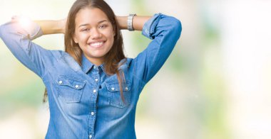 Üzerinde mavi kot gömlek giyen genç güzel esmer kadın izole arka plan rahatlatıcı ve kollar ve eller baş ve boyun, mutlu gülümseyerek arkasında ile germe