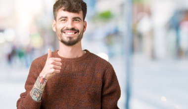 Hareketi el ile mutlu yaşasın yapıyor izole arka plan üzerinde kış kazak giyen genç yakışıklı adam. Başarı gösteren kameraya bakarak ifade onaylama.