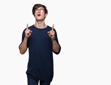 Yakışıklı delikanlı hayrete ve yukarıya bakıyor ve parmakları ile işaret ve silah kaldırdı sürpriz izole arka plan üzerinde gözlük.