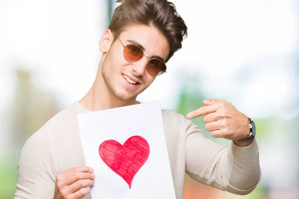 Joven Hombre Guapo Sosteniendo Tarjeta Con Corazón Rojo Sobre Fondo — Foto de Stock