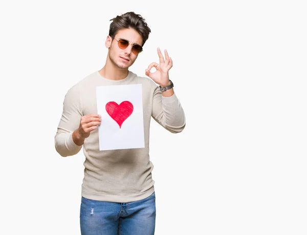 Joven Hombre Guapo Sosteniendo Tarjeta Con Corazón Rojo Sobre Fondo — Foto de Stock