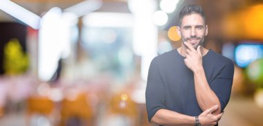 Emin çapraz kollar ve çeneme kaldırdı el ile gülümseme ile kameraya bakarak izole arka plan üzerinde kazak giyen genç yakışıklı adam. Pozitif düşünce.