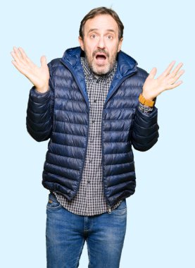 Kış ceket clueless ve şaşkın bir ifadeyle kollar ve eller kaldırdı giyen orta yaş yakışıklı adam. Şüphe kavramı.
