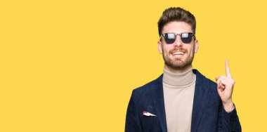 Genç yakışıklı zarif adam başarılı fikirle parmak işaret güneş gözlüğü takıyor. Çıktıktan ve mutlu. Bir numara.