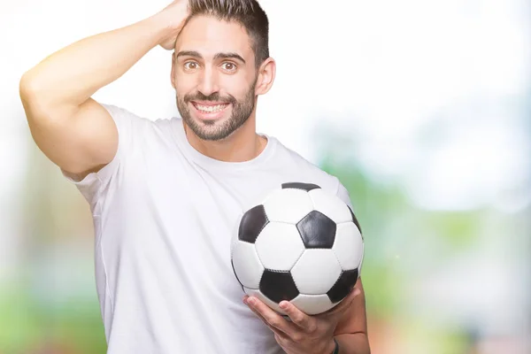 サッカー サッカー ボールの頭の上の手を強調した分離の背景の上に保持している若い男が恥と驚きの顔でショックを受けて怒っているとイライラします 恐怖と動揺の間違い — ストック写真