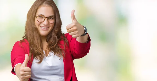 Beautiful plus size young business woman wearing elegant jacket and glasses over isolated background approving doing positive gesture with hand, thumbs up smiling and happy for success. Looking at the camera, winner gesture.