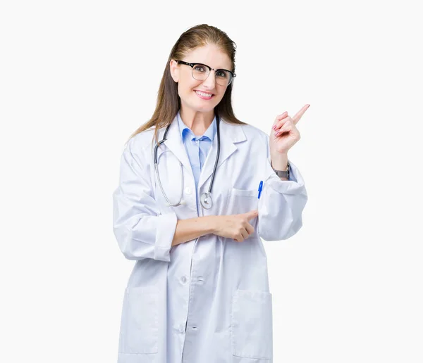 中年成熟的医生妇女穿着医疗外套在孤立的背景与灿烂的笑容在脸上 用手和手指指着一边看着镜头 — 图库照片