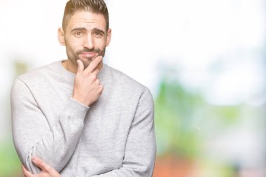 Emin çapraz kollar ve çeneme kaldırdı el ile gülümseme ile kameraya bakarak izole arka plan üzerinde kazak giyen genç yakışıklı adam. Pozitif düşünce.