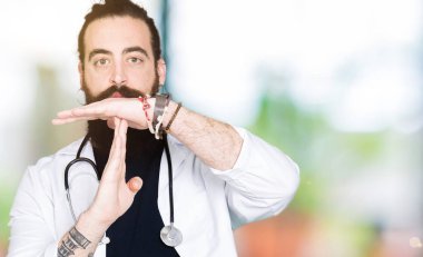 Doktor uzun saçlı tıbbi ceket ve stetoskop yapıyor zaman aşımı jest elle, sinirli ve ciddi bir yüz