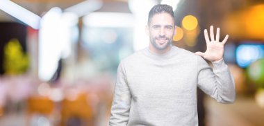 Gösterilen arka plan üzerinde sweatshirt giyen genç yakışıklı adam izole ve parmakları ile işaret kendinden emin ve mutlu gülümseyerek süre beş numara.