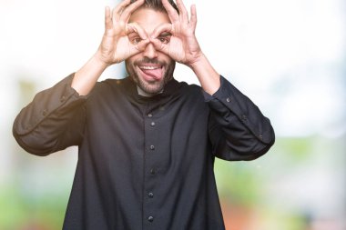 Genç Hıristiyan rahip dilini, parmaklarının arasından baktığını yapışmasını dürbün gibi ok jest yapıyor izole arka plan üzerinde. Deli ifade.